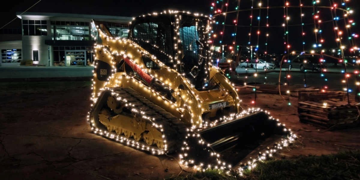 Minicargador amarillo decorado con luces blancas por la noche junto a un edificio y autos estacionados