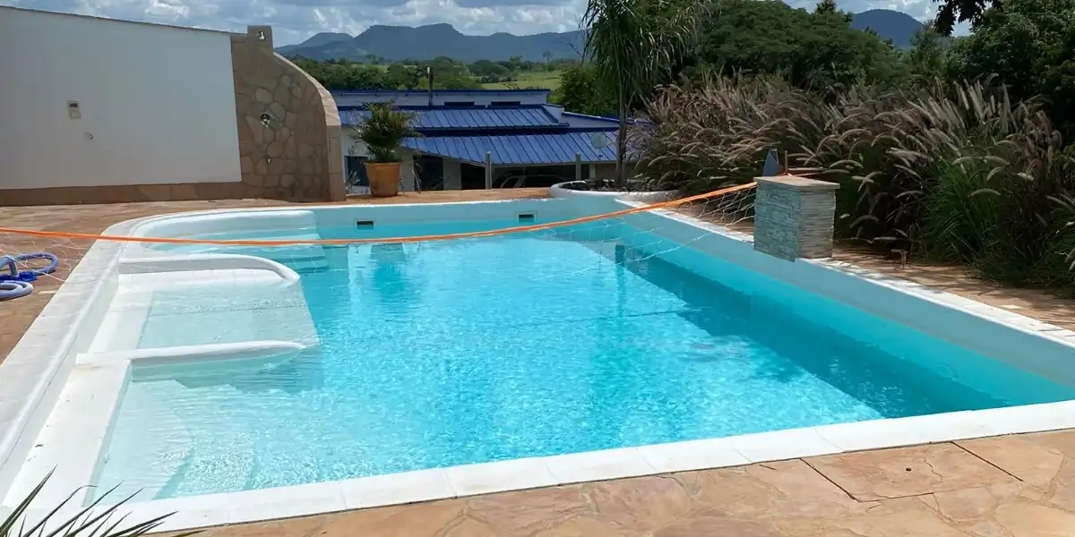 Piscina exterior rectangular con agua clara, deck de piedra, edificios con techo azul y montañas al fondo