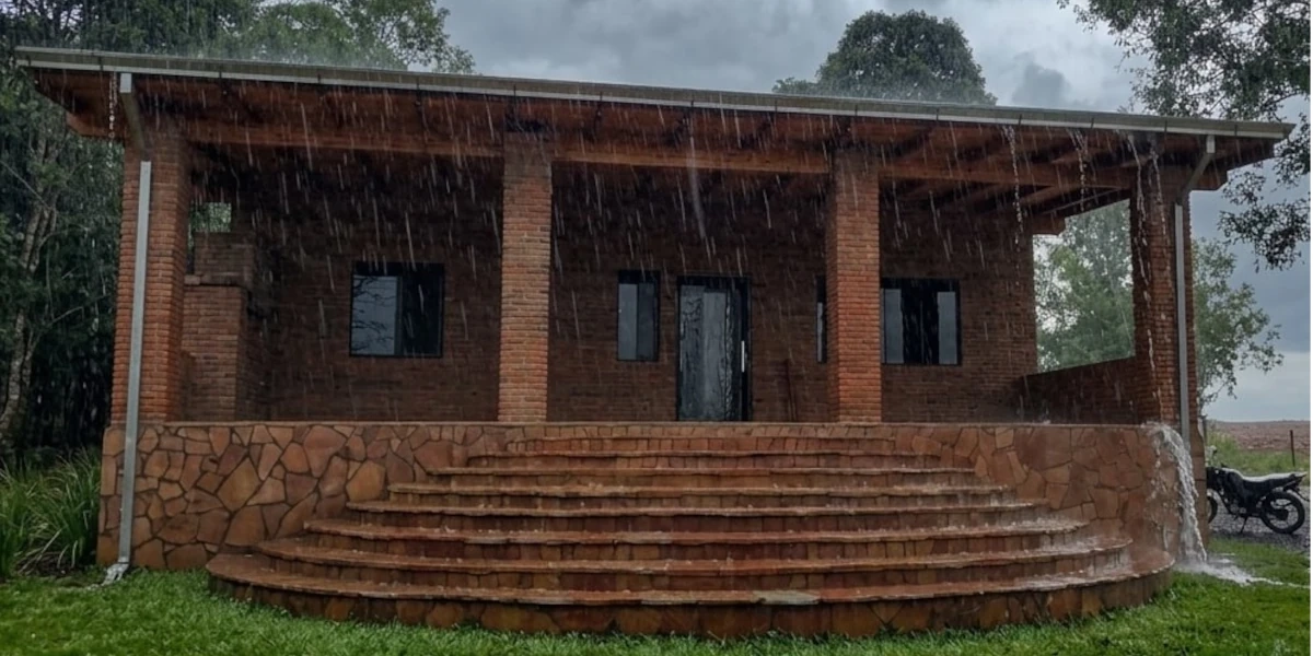 Lluvia intensa sobre un techo de tejas en Paraguay con una canaleta desbordada y fachada mojada